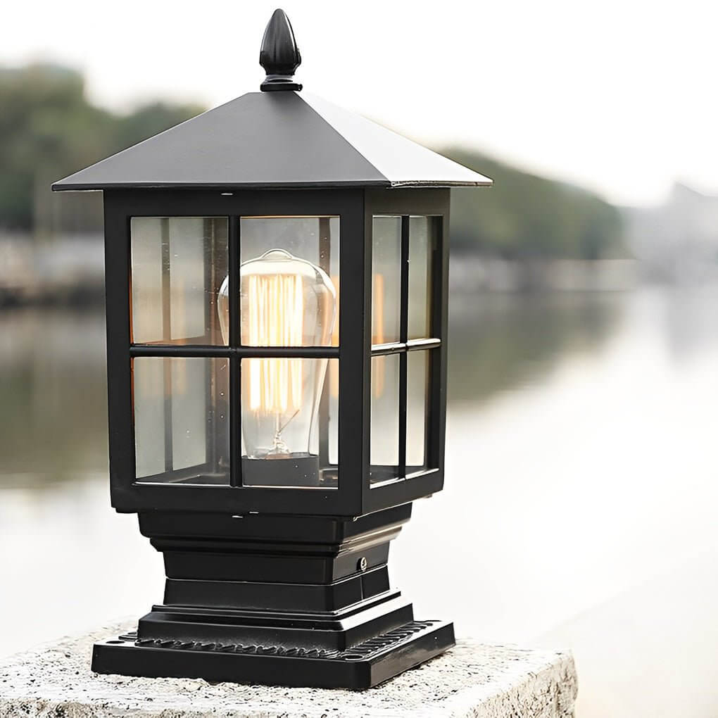 Stone light pillar with a black lantern, casting warm illumination near a stone wall.