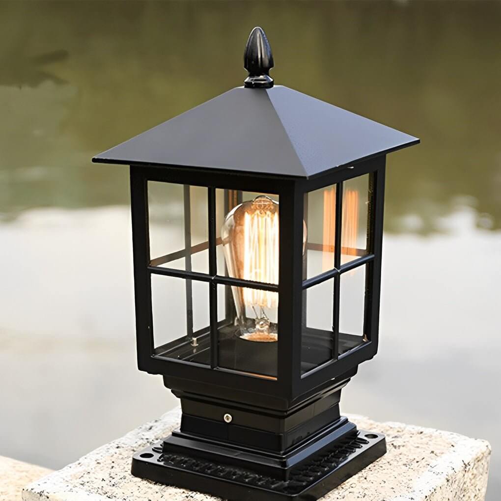 Stone light pillar with a black lantern, casting warm light near a modern building.