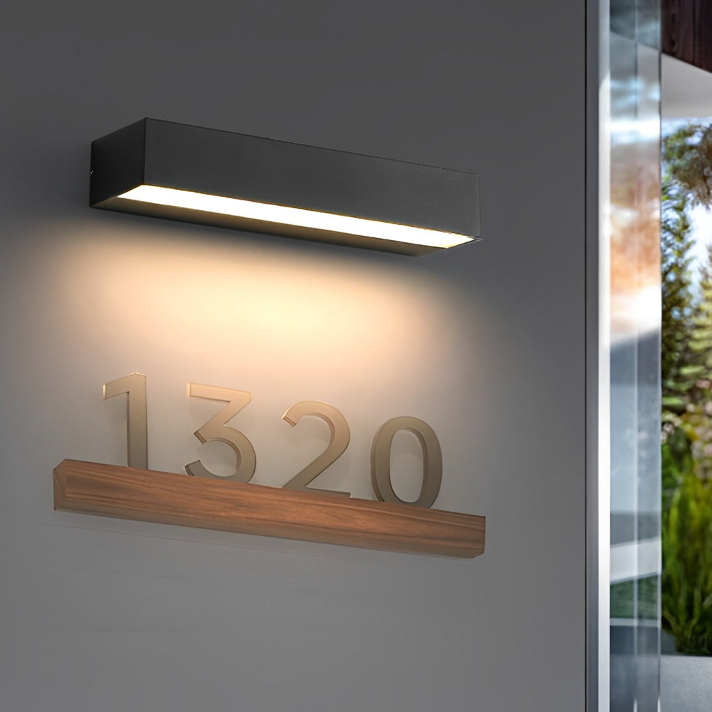 Exterior porch light fixtures illuminating house number plaque and entry wall at night.