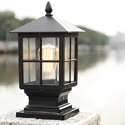 Stone light pillar with a black lantern, casting warm illumination near a stone wall.